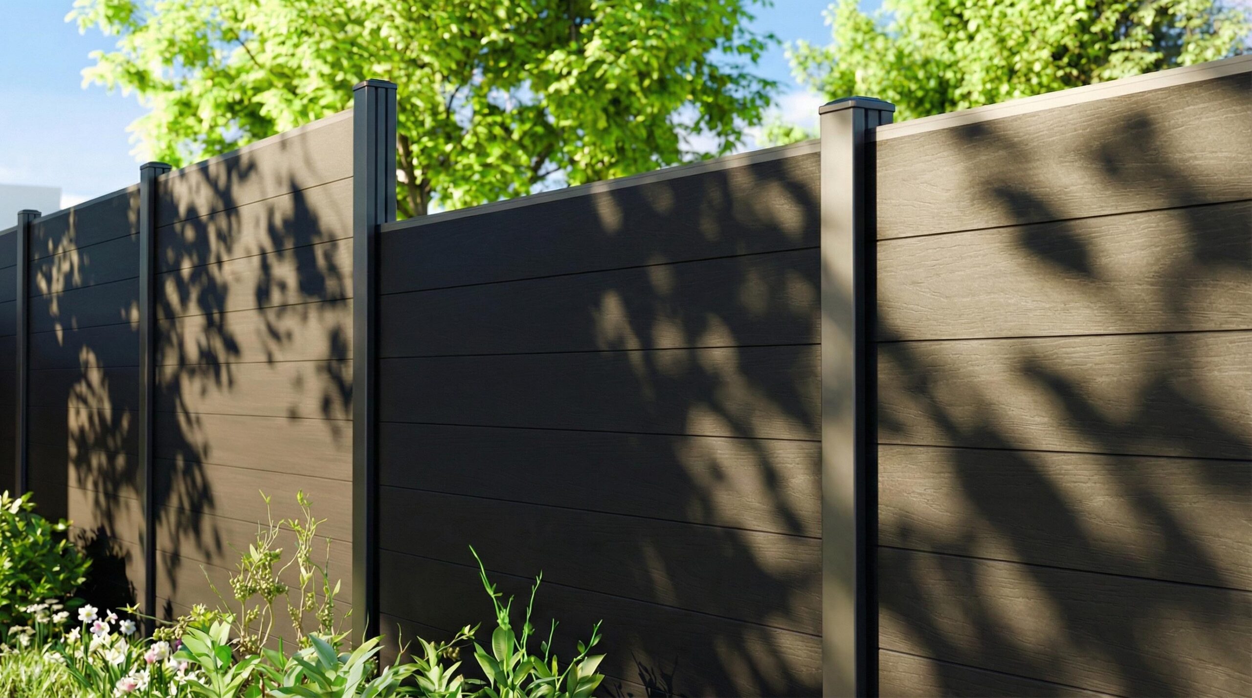Charcoal wood-look composite privacy fence with horizontal panels and dark metal posts, bordered by greenery in dappled sunlight.